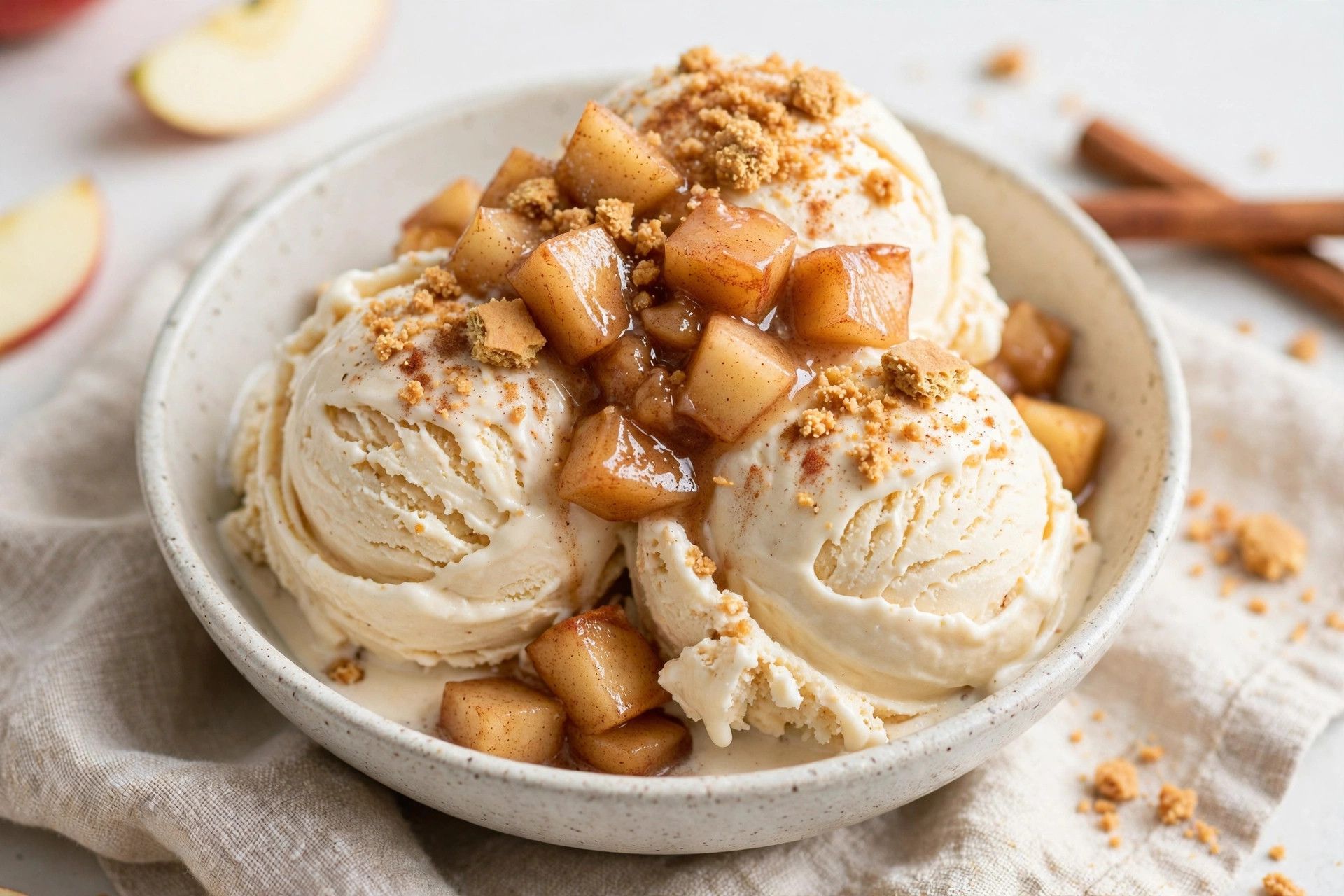 A bowl of thick apple pie protein ice cream scoops with tender cinnamon apple pieces and graham cracker crumbles, on a light kitchen table