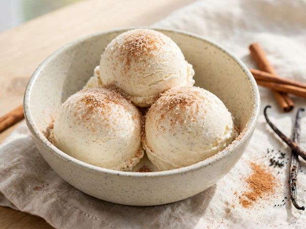 A bowl of cinnamon vanilla churro protein ice cream scoops dusted with cinnamon sugar, on a light kitchen table