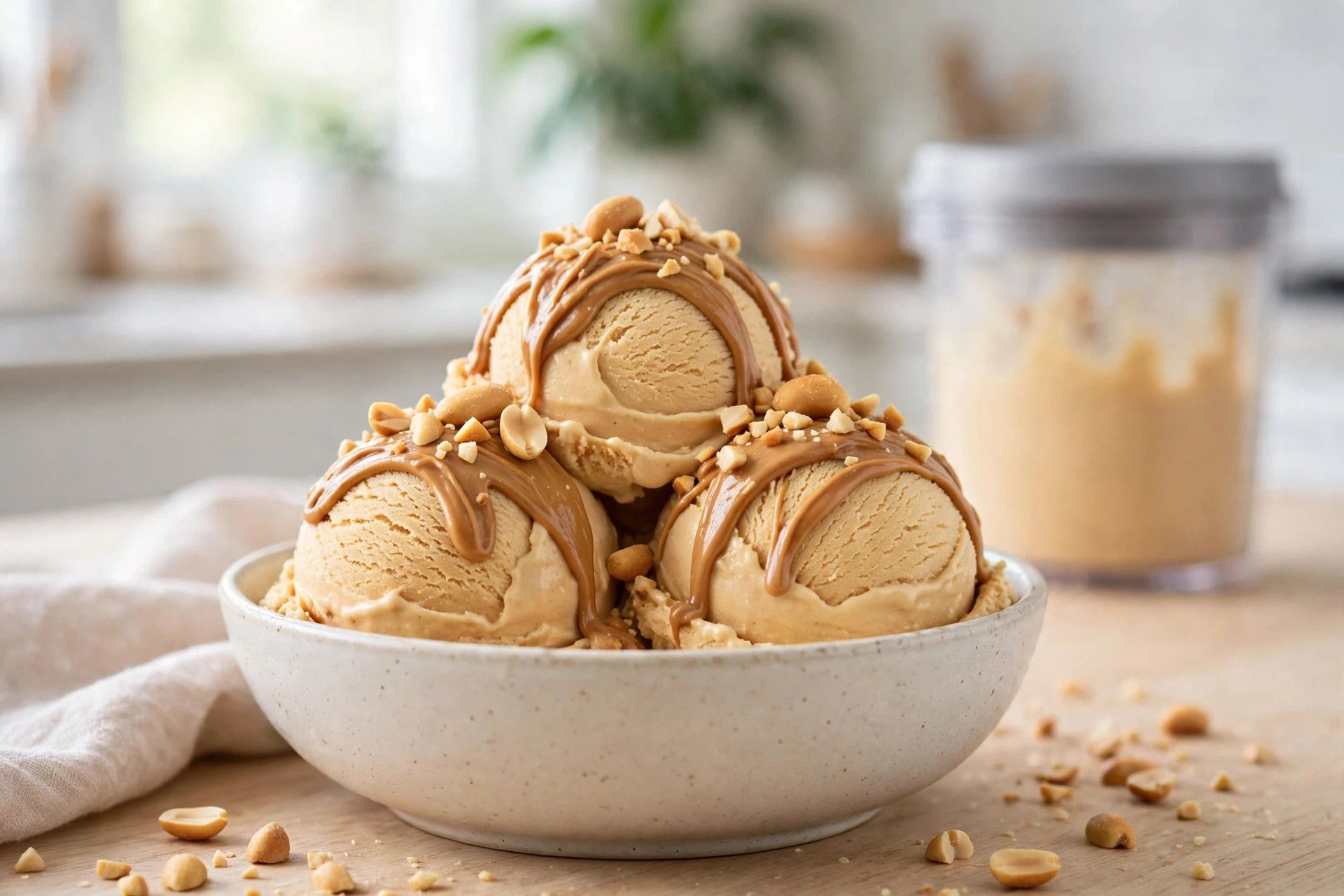 A bowl of thick peanut butter ice cream scoops with a peanut butter drizzle and chopped roasted peanuts on top