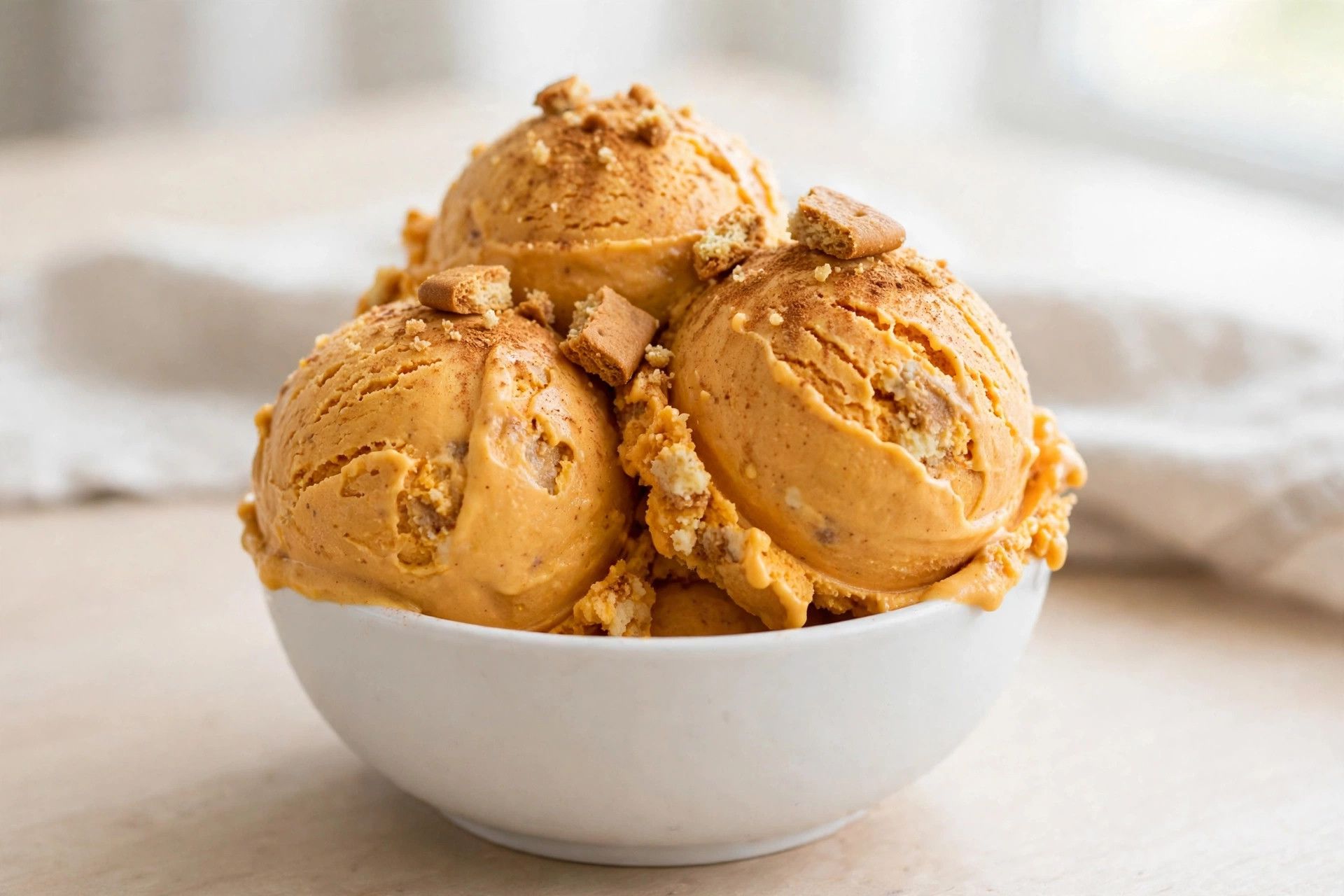 A bowl of pumpkin cheesecake ninja creami scoops, warm orange and creamy, dusted with cinnamon on a light table